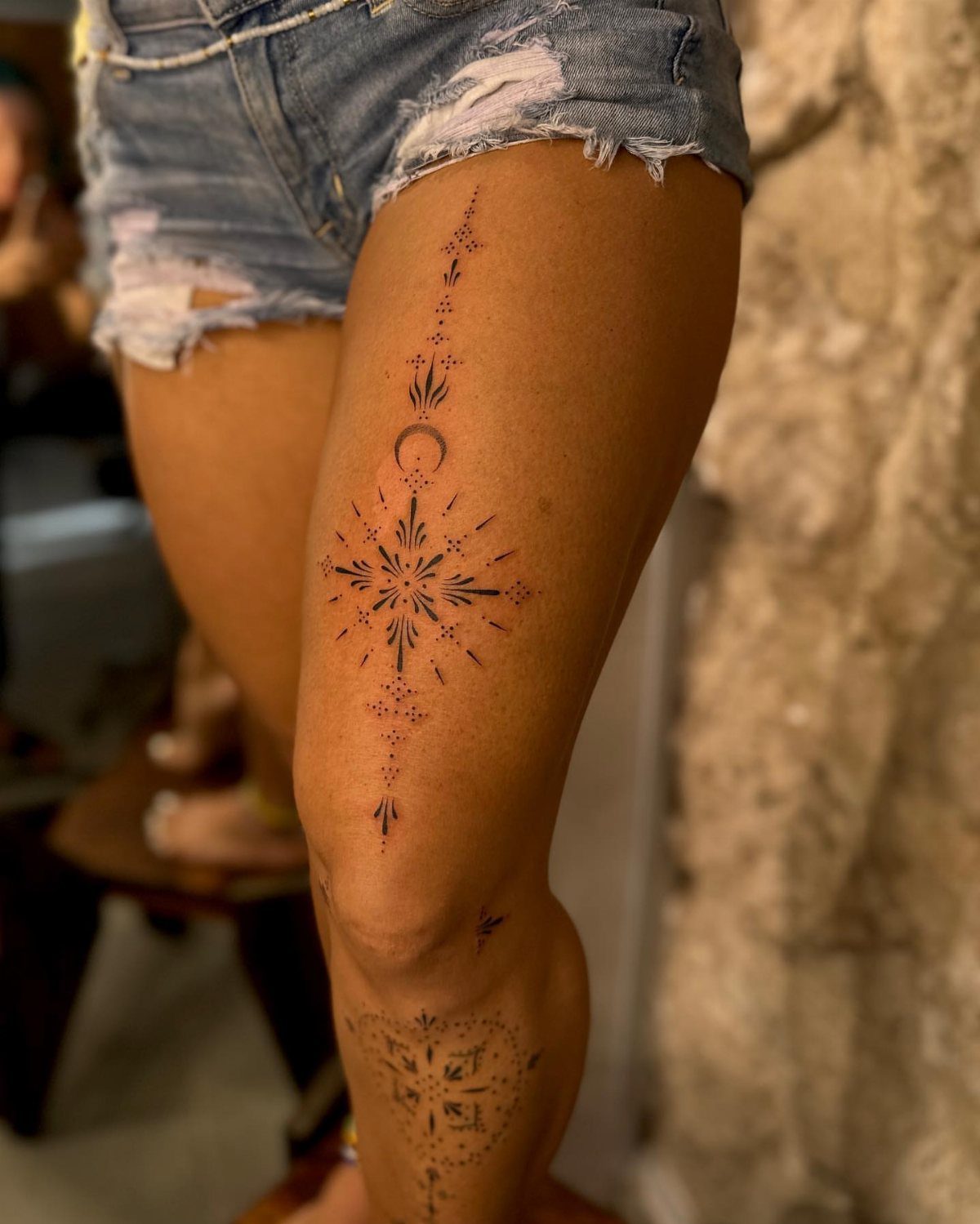Thigh Tattoos for Women: 8 Ideas from Floral to Geometric Art 7 A black ink geometric starburst and crescent moon tattoo on a woman's thigh.