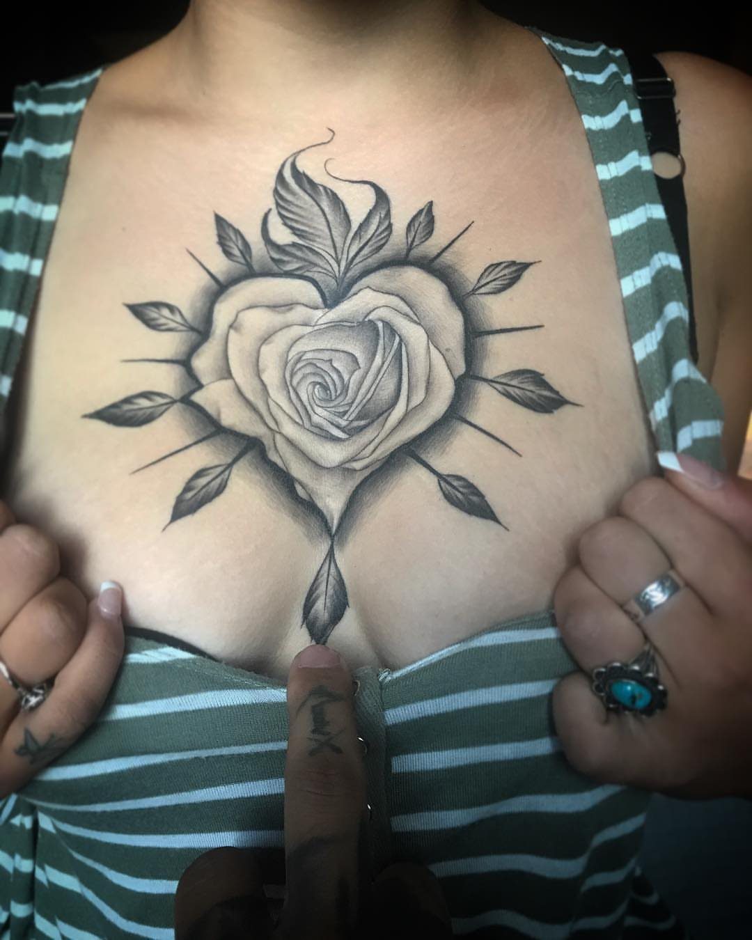 9 Chest Tattoo Ideas for Women: Floral, Sternum, Underboob & More 2026 10 A rose shaped like a heart tattooed on a woman's chest with leaves and rays.