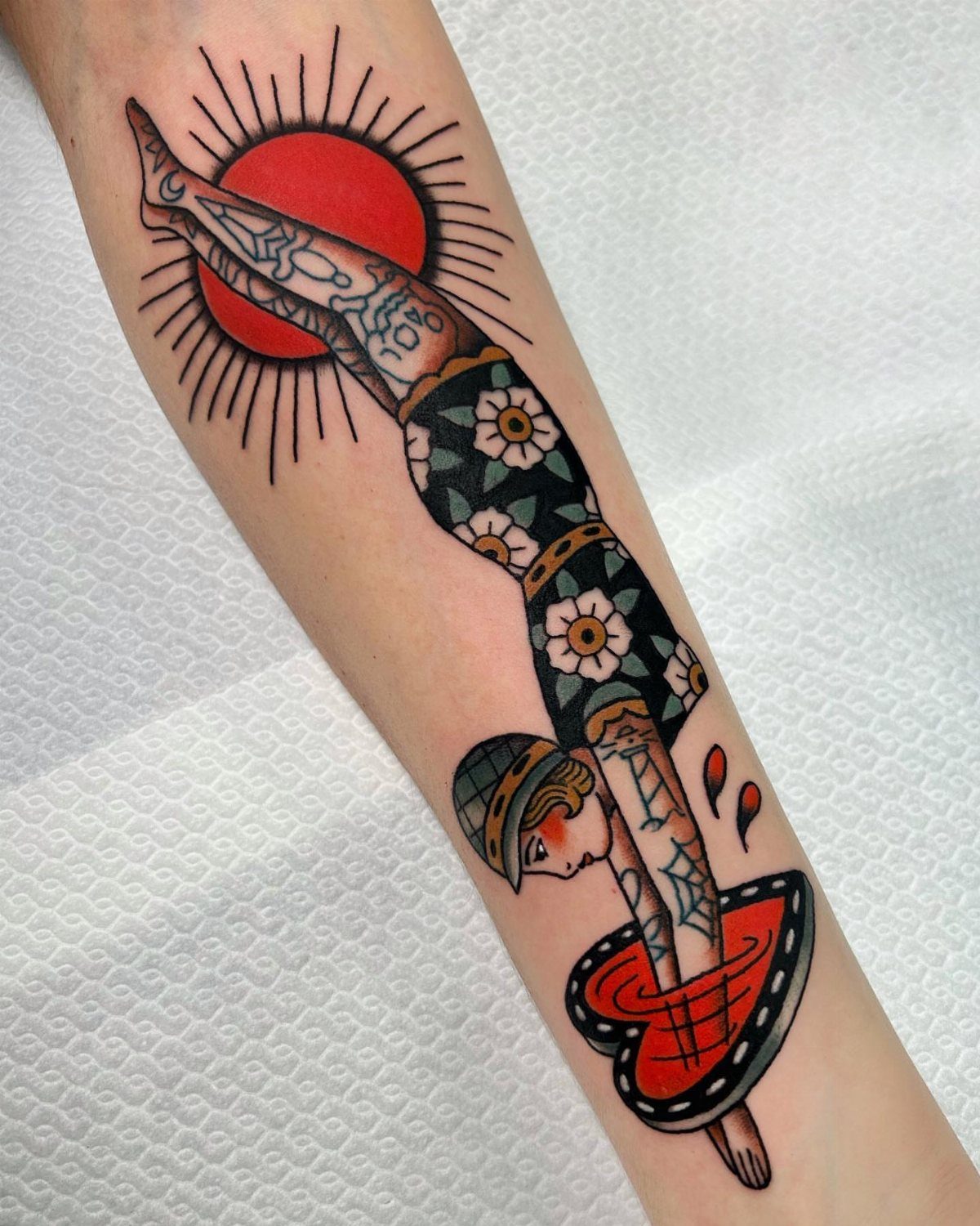 An American traditional tattoo of a woman doing a handstand against a red sun on an arm.