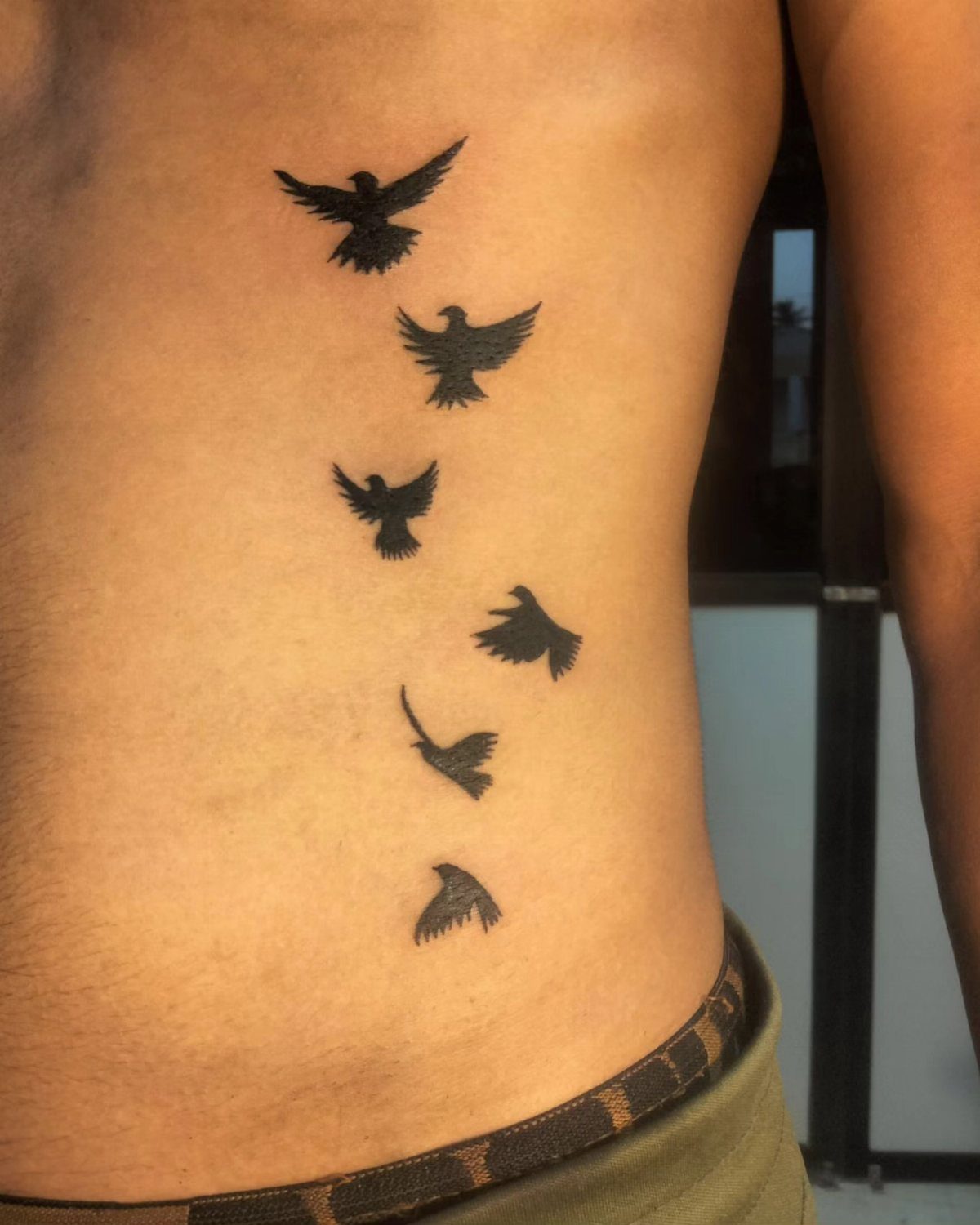 Black bird silhouette tattoos in flight on a man's side and abdomen.