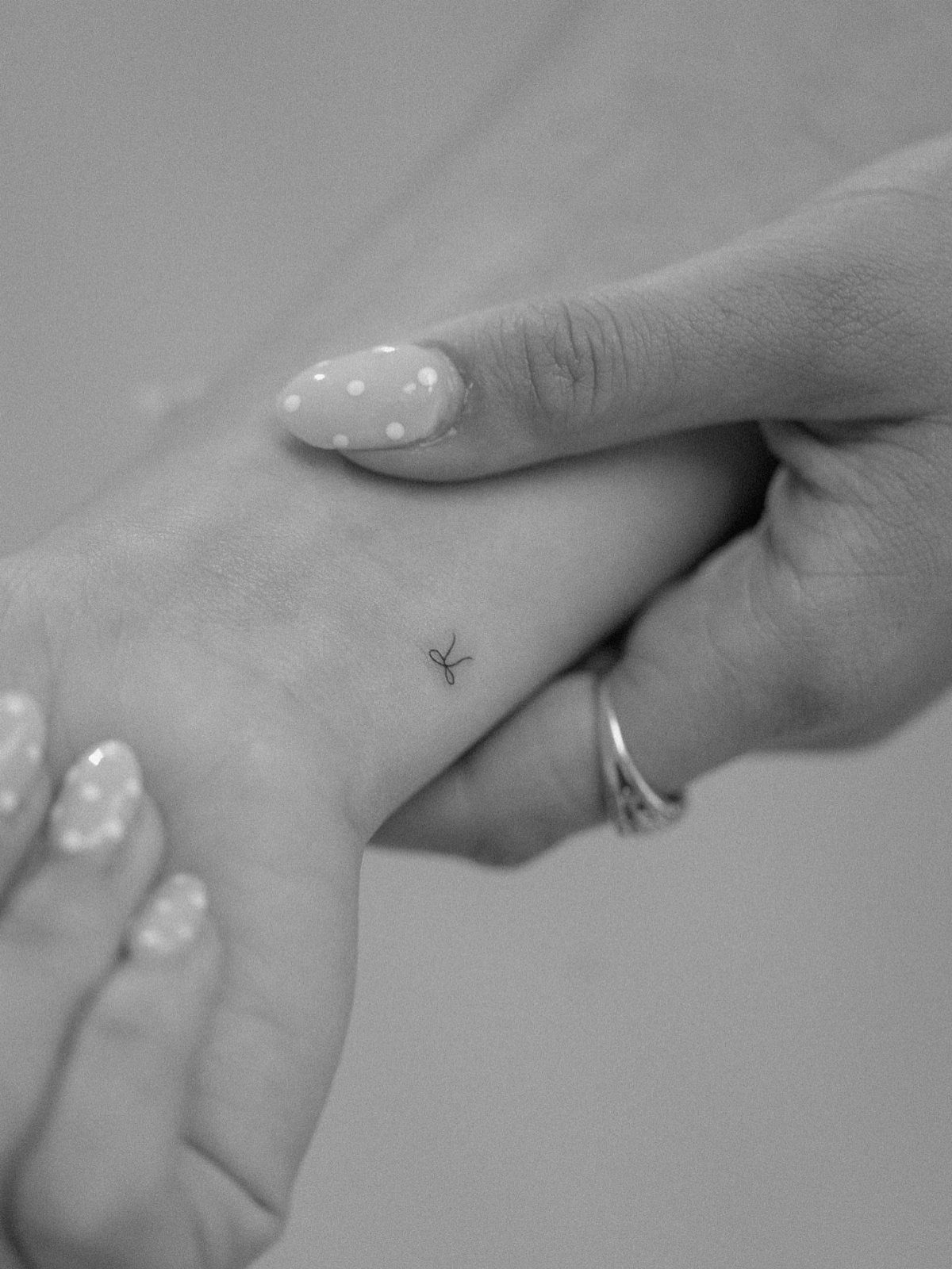 A tiny bow tattoo on the side of a person's finger with polka dot nail art.