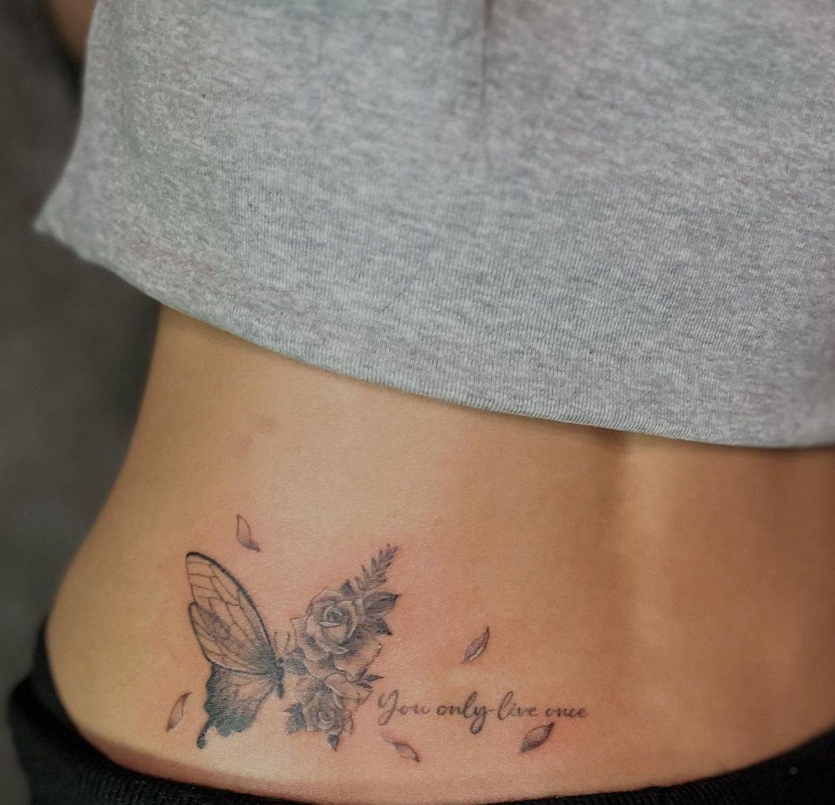 A butterfly and rose tattoo with script text on a person's lower side back.