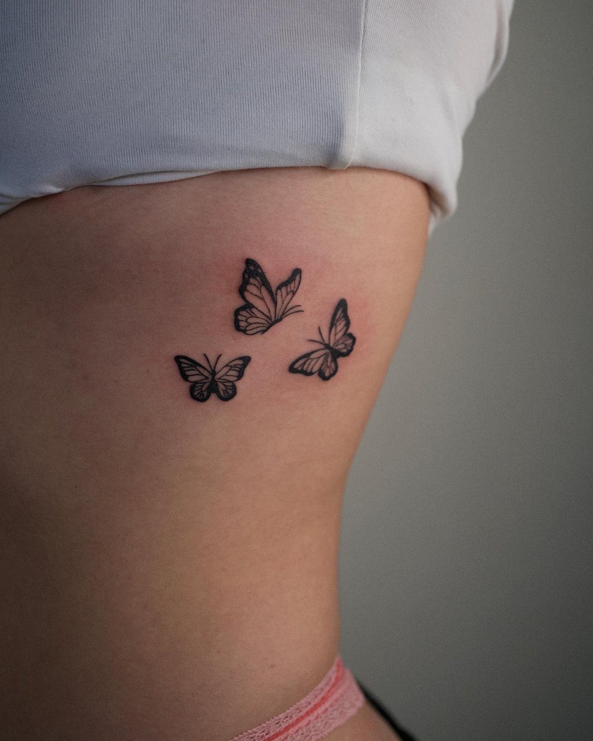 Three small black butterfly tattoos on a person's side ribcage.