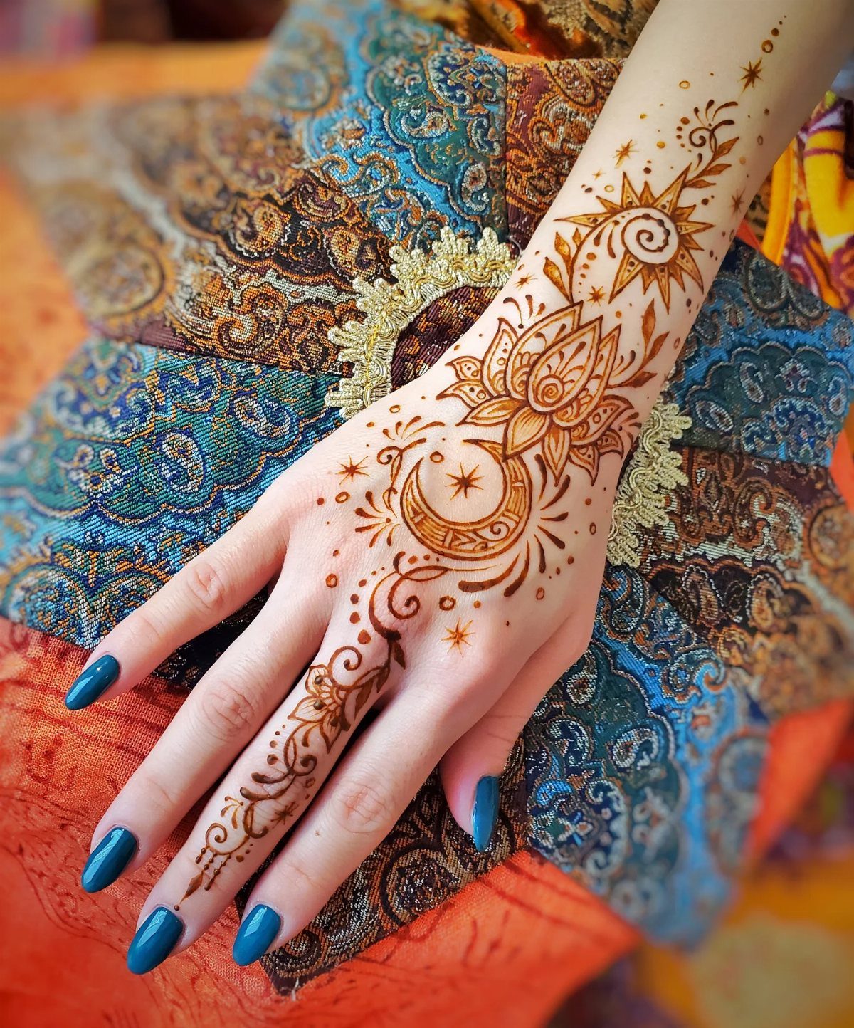 A hand decorated with celestial henna designs including a crescent moon, stars, and sun motifs.