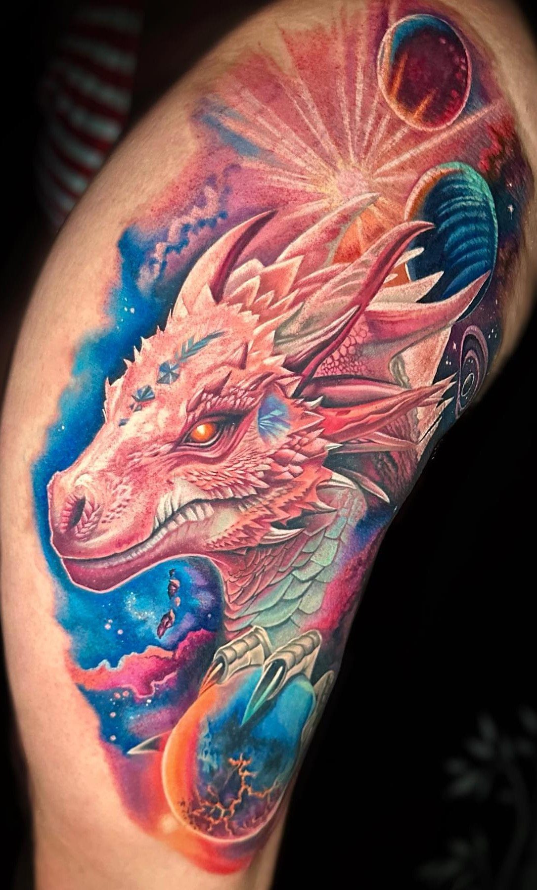 A vibrant pink dragon tattoo surrounded by colorful planets and celestial cosmic nebulae on skin.