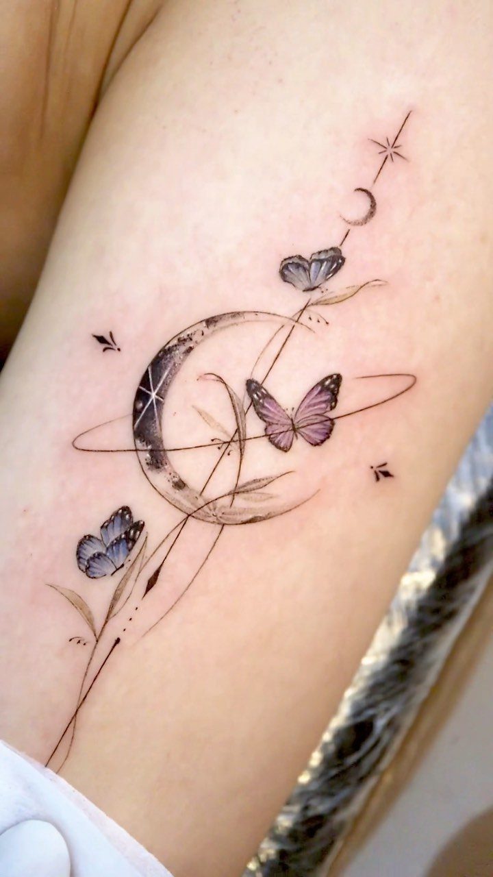 A celestial tattoo on skin featuring a crescent moon, butterflies, and fine lines.
