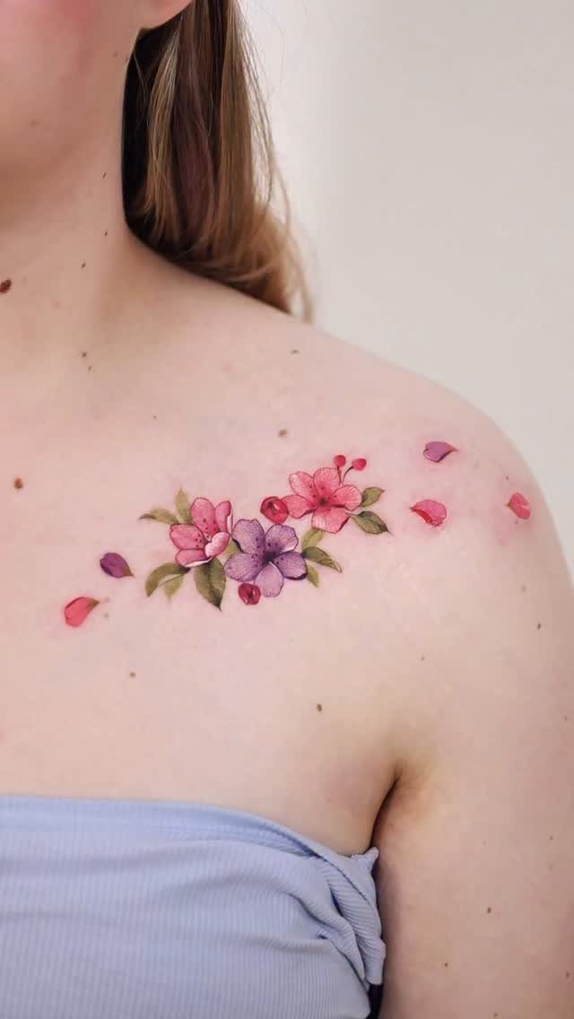 A colorful cherry blossom tattoo with pink and purple flowers on a person's shoulder.