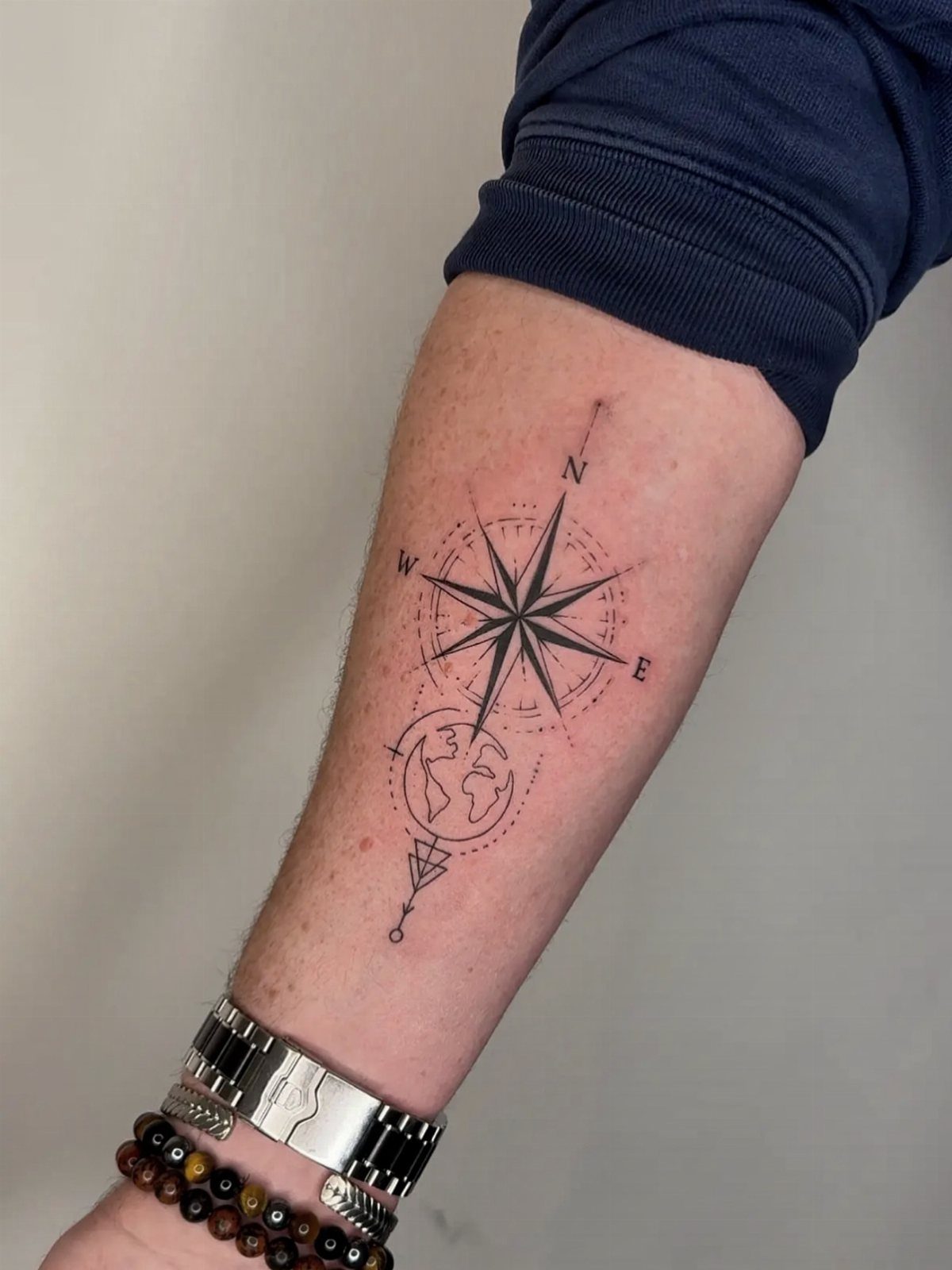 Fine Line Travel Tattoo: 10 Designs That Stay Light on Skin 3 A fine line tattoo of a compass rose and world map on a person's forearm.