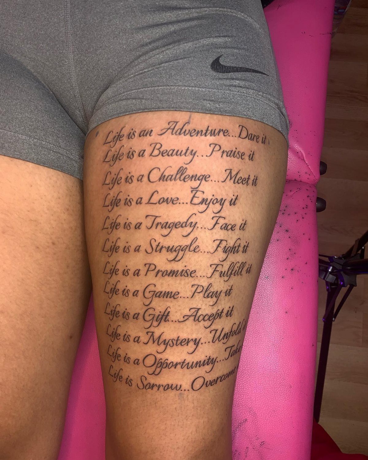 Thigh Tattoos for Women: 8 Ideas from Floral to Geometric Art 5 A large tattoo of multiple lines of cursive script text on a person's thigh.