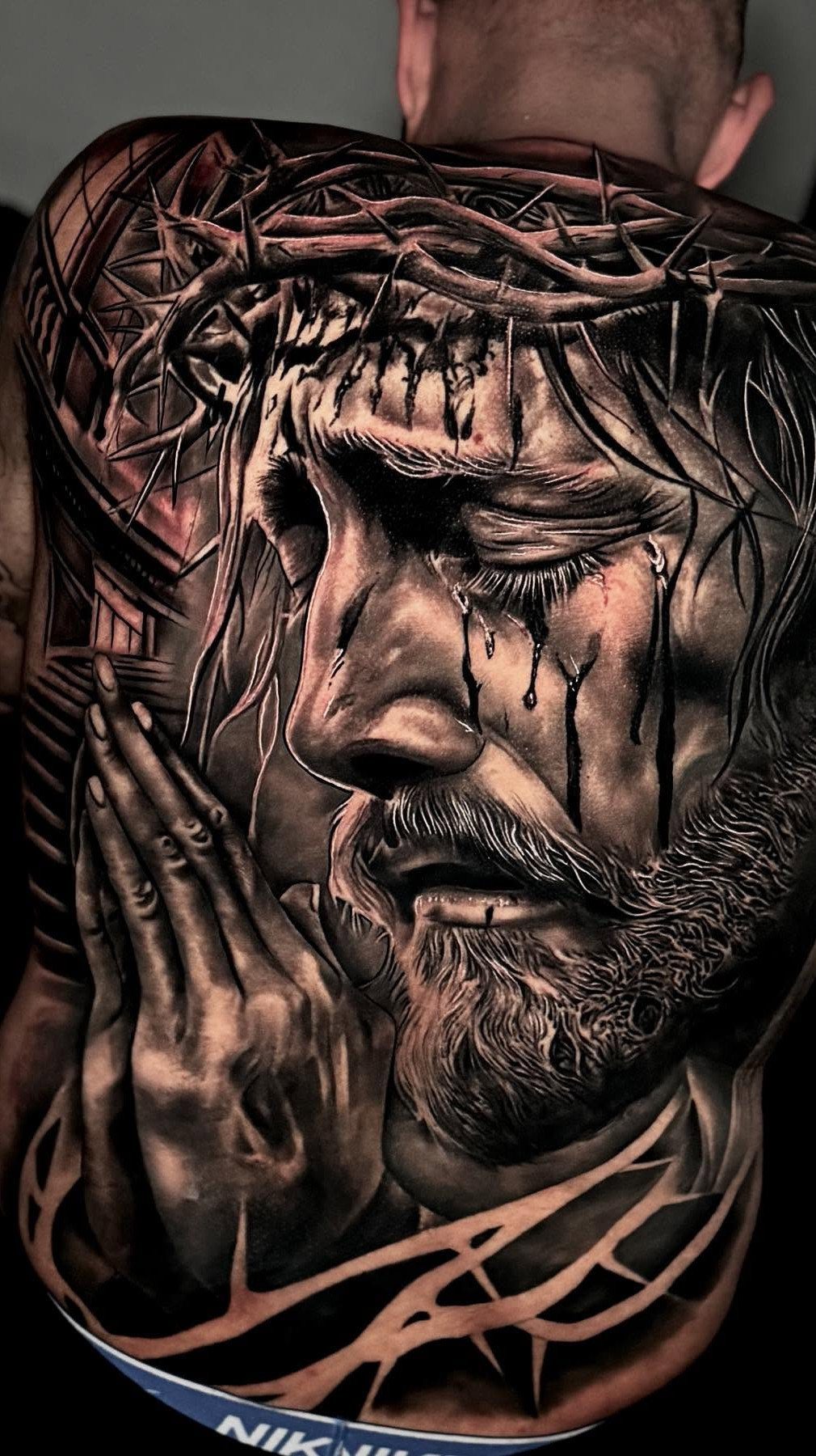 Back Pieces Tattoo: 7 Designs That Use the Whole Canvas 3 A detailed black and grey realism tattoo of a praying man with a crown of thorns.