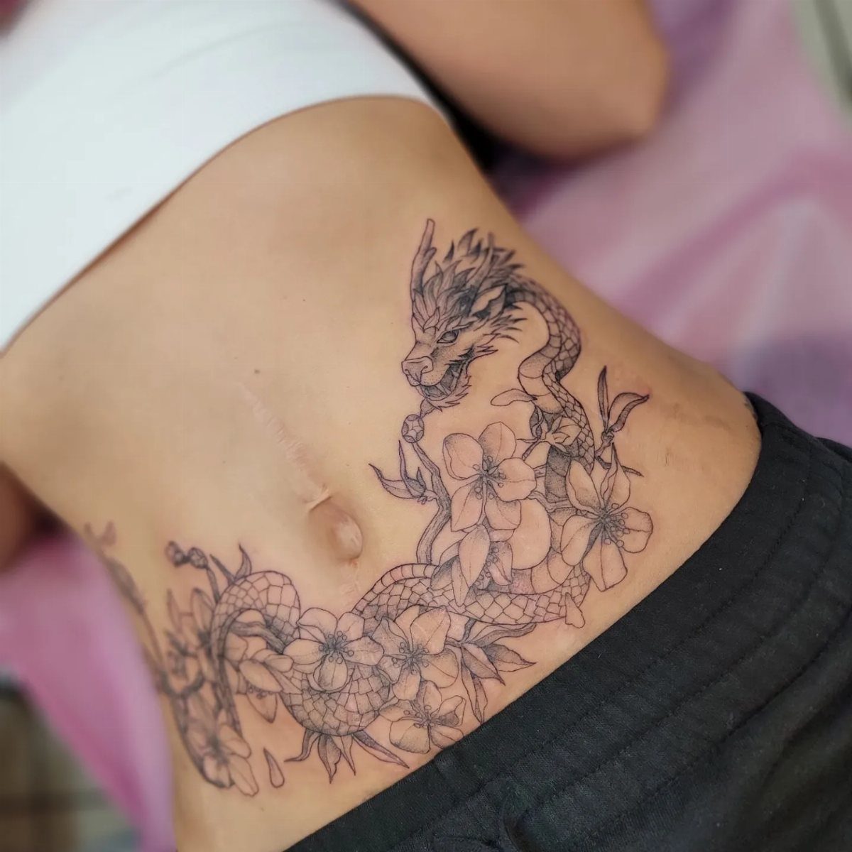 Tattoo Placement: 8 Lower Stomach Ideas for Your Next Ink 7 A large dragon and cherry blossom tattoo on a person's lower stomach and hip.