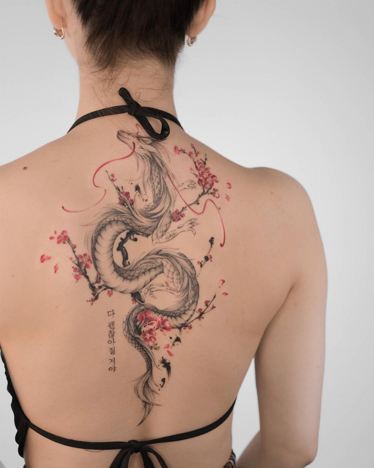 6 Dragon Backpiece Tattoo Ideas for Your Next Session 3 A large black ink dragon tattoo with pink cherry blossoms on a person's back.