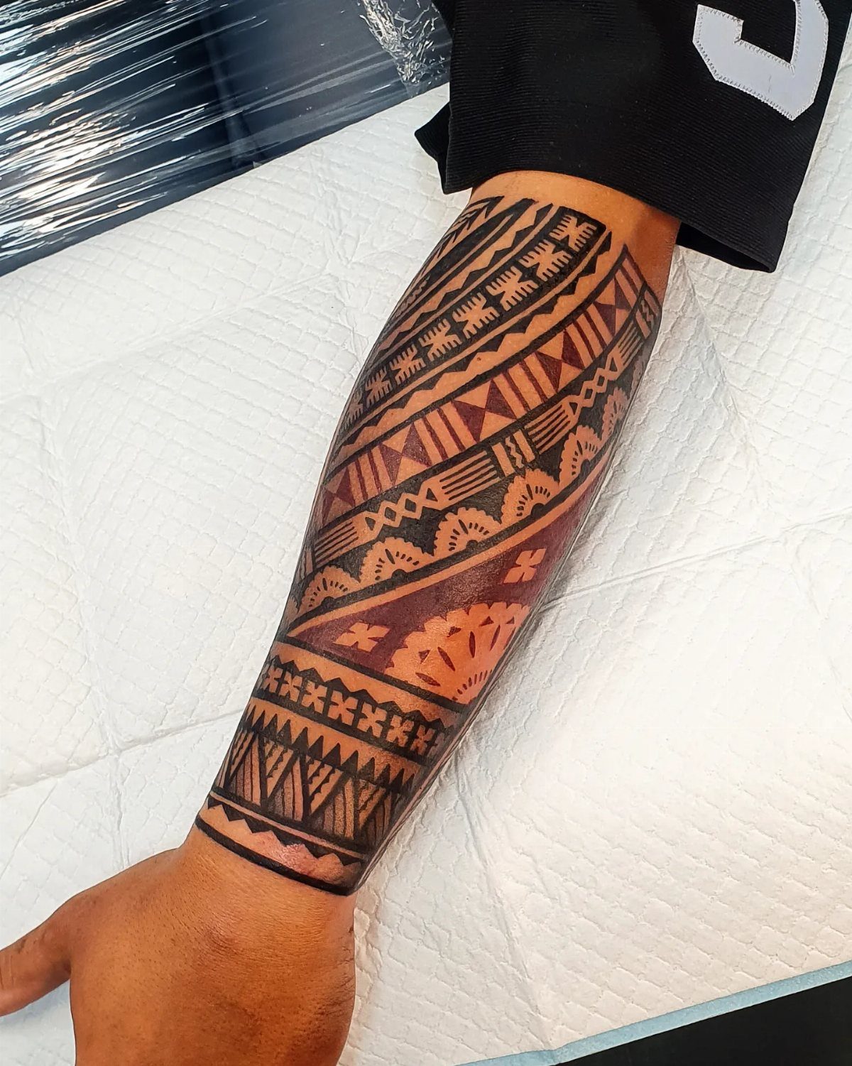 Polynesian Tattoo Pattern: 16 Island Styles From Marquesan to Maori 7 A person's forearm covered in a detailed black ink Polynesian tattoo with geometric patterns.