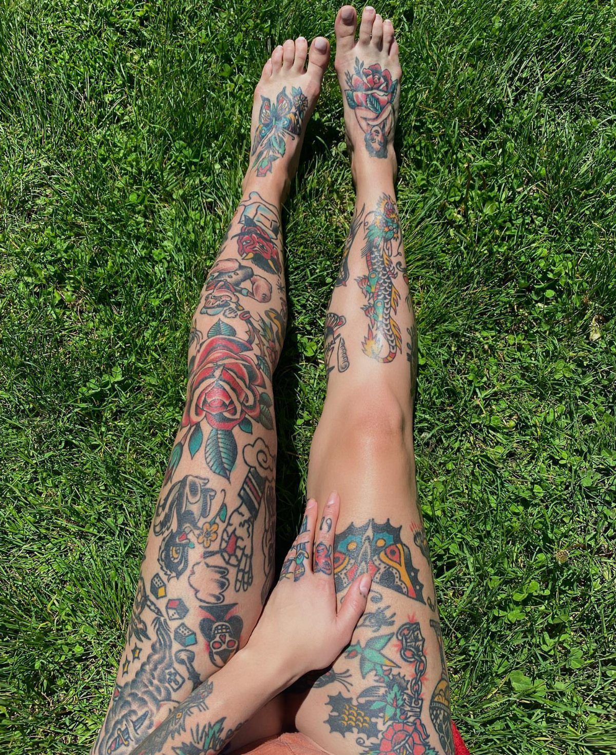 Tattooed legs and feet resting on green grass showing various American traditional style designs.