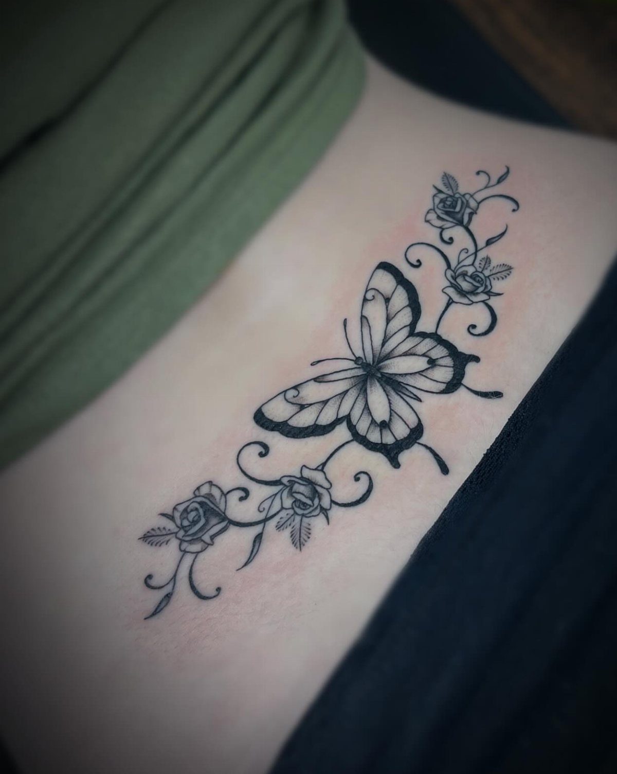 A black ink butterfly and rose tattoo on a person's side skin.