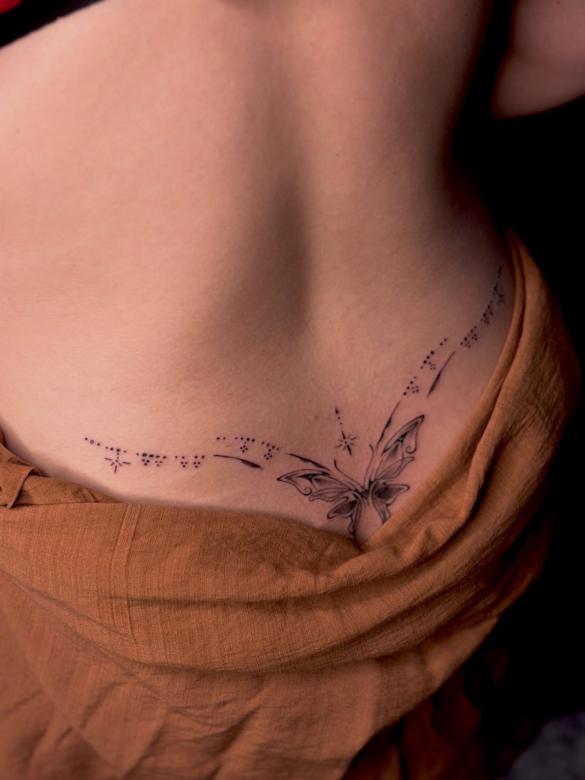 A delicate butterfly tattoo with fine line details on a person's lower side back.
