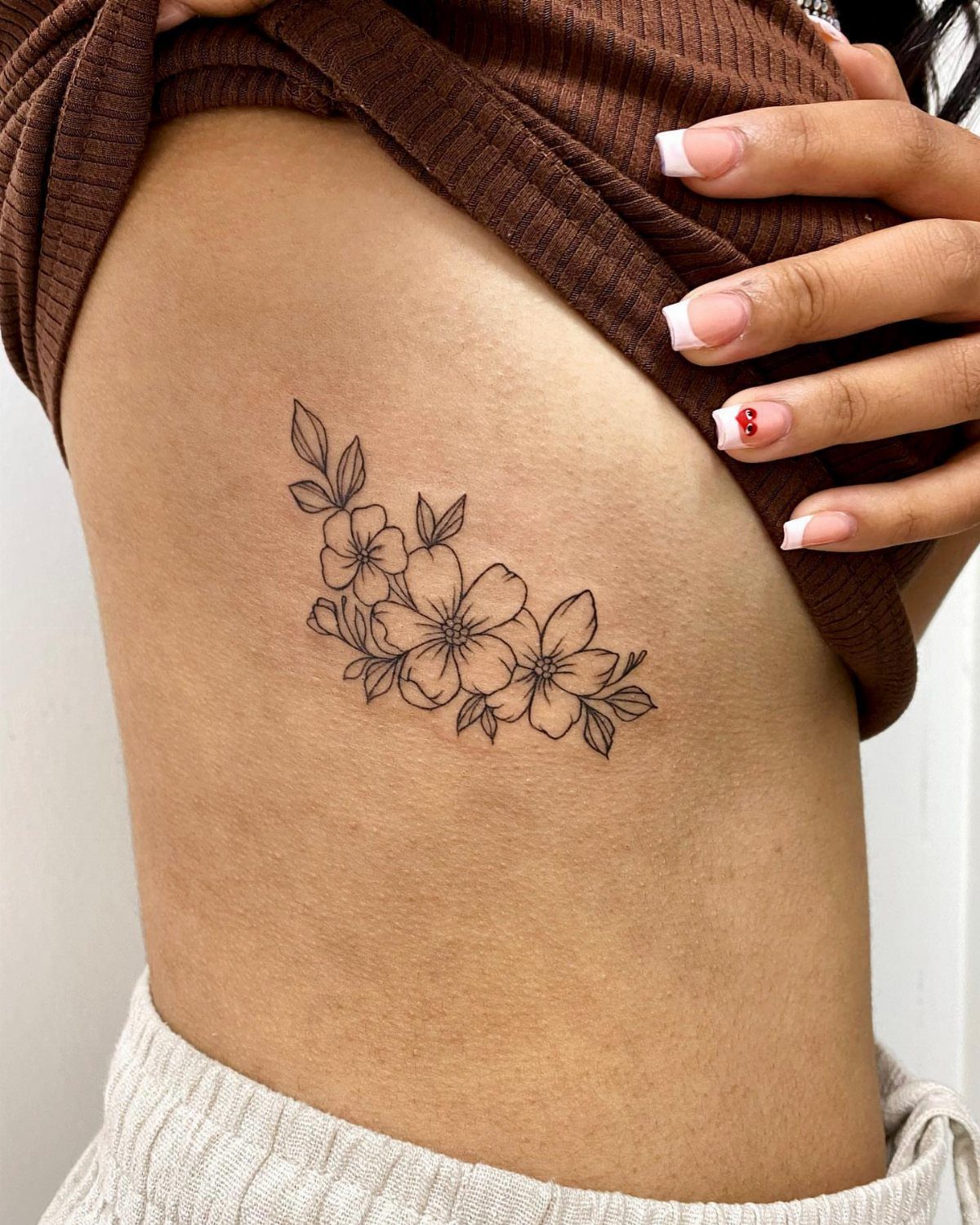 A delicate black ink floral tattoo on a person's side ribcage area.