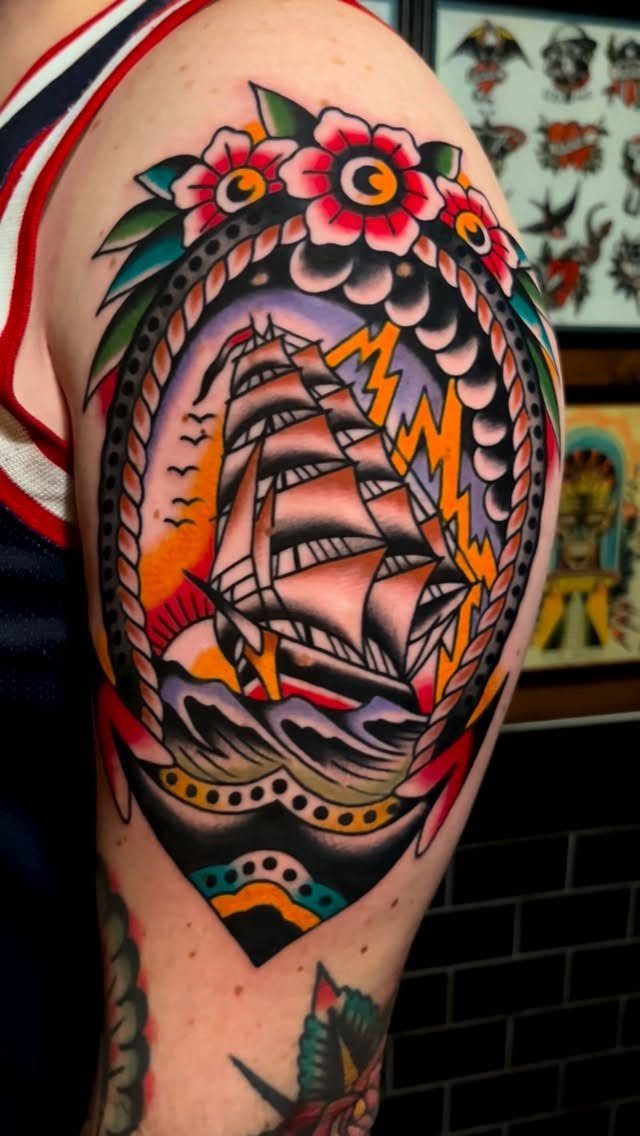 A colorful American traditional tattoo of a sailing ship surrounded by red roses on a person's shoulder.