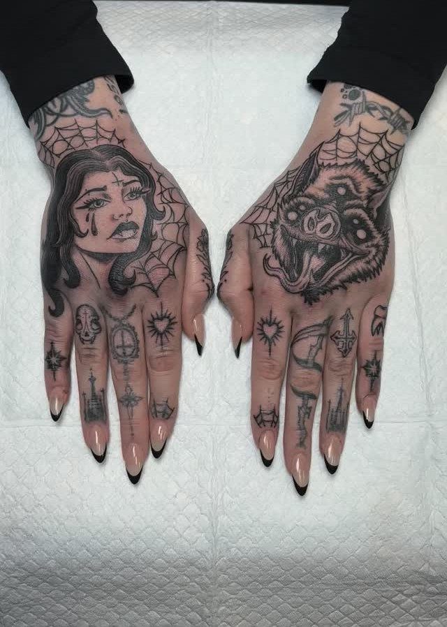 Two hands covered in detailed black and grey tattoos featuring faces and spiderwebs.