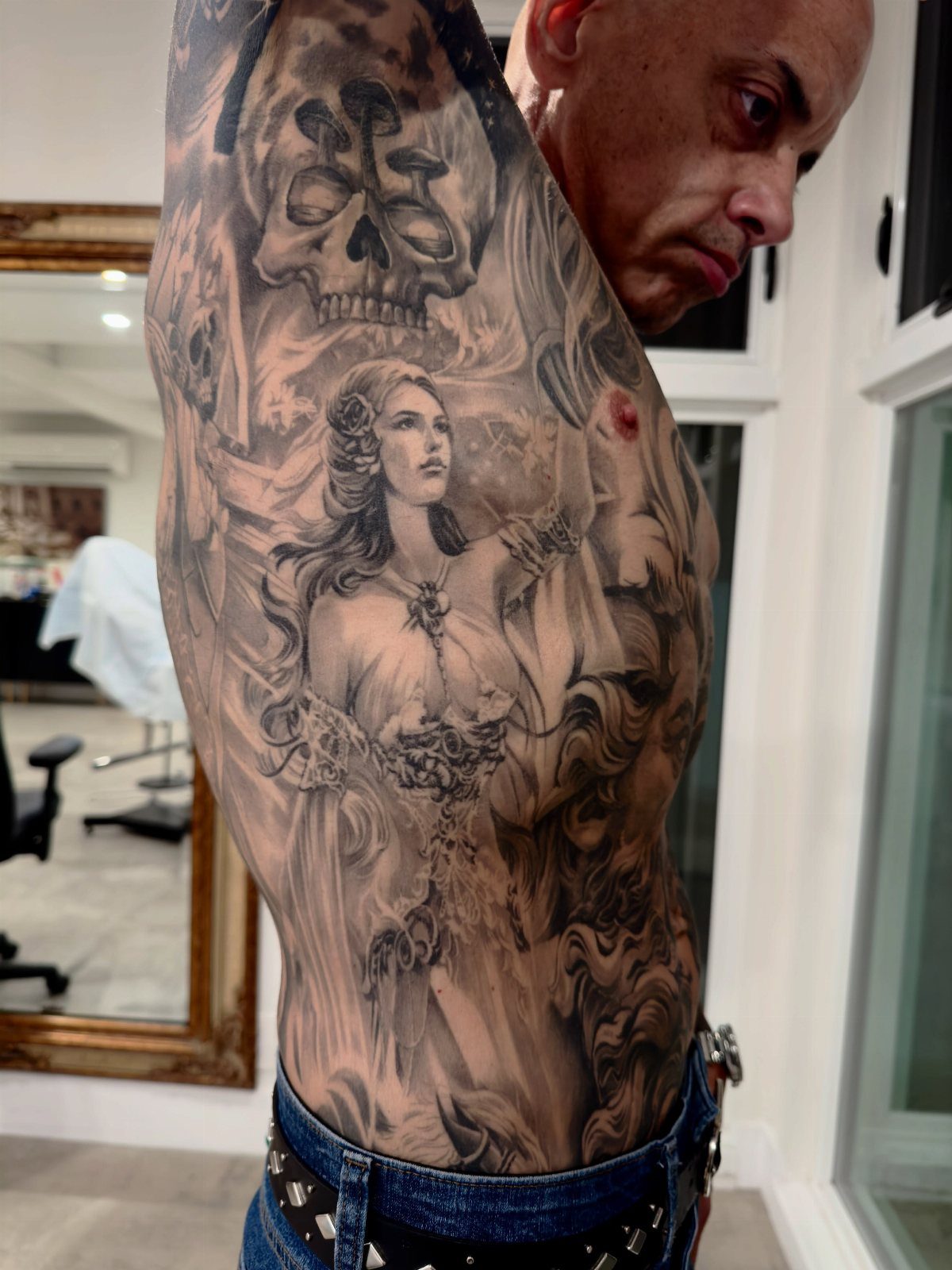 A man displaying a large, detailed black and grey realism tattoo covering his entire ribcage.