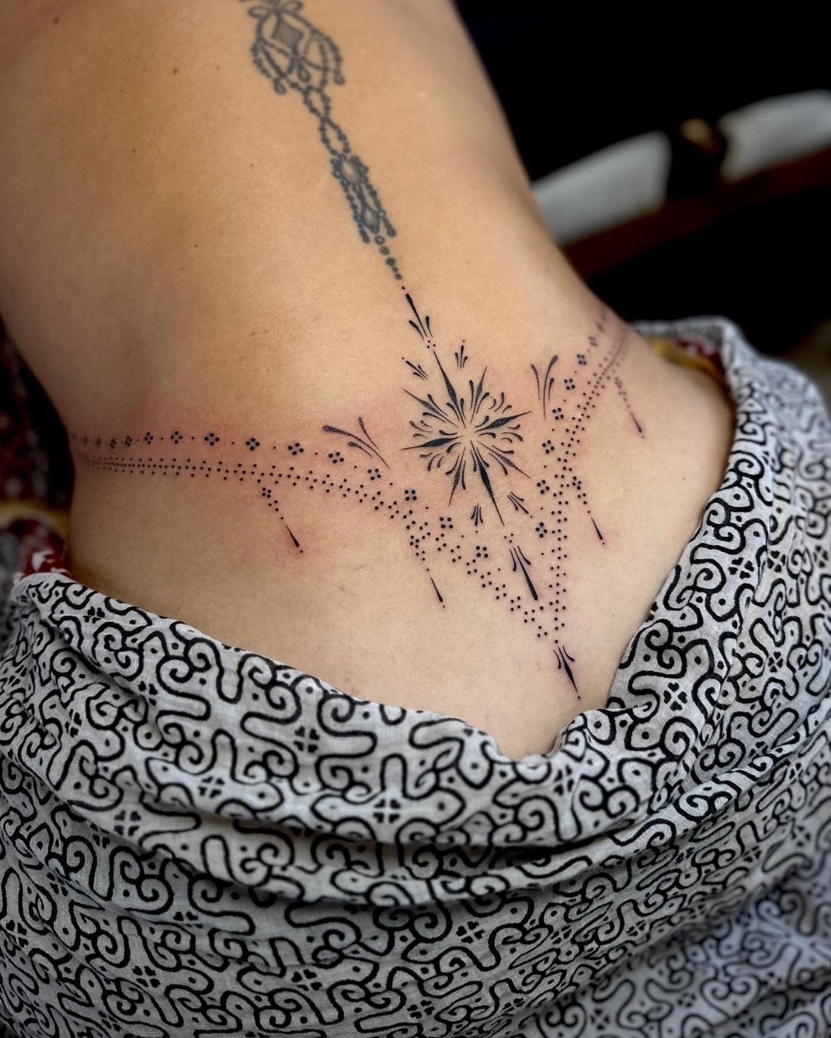 A delicate black ink geometric tattoo design on a person's lower back skin.