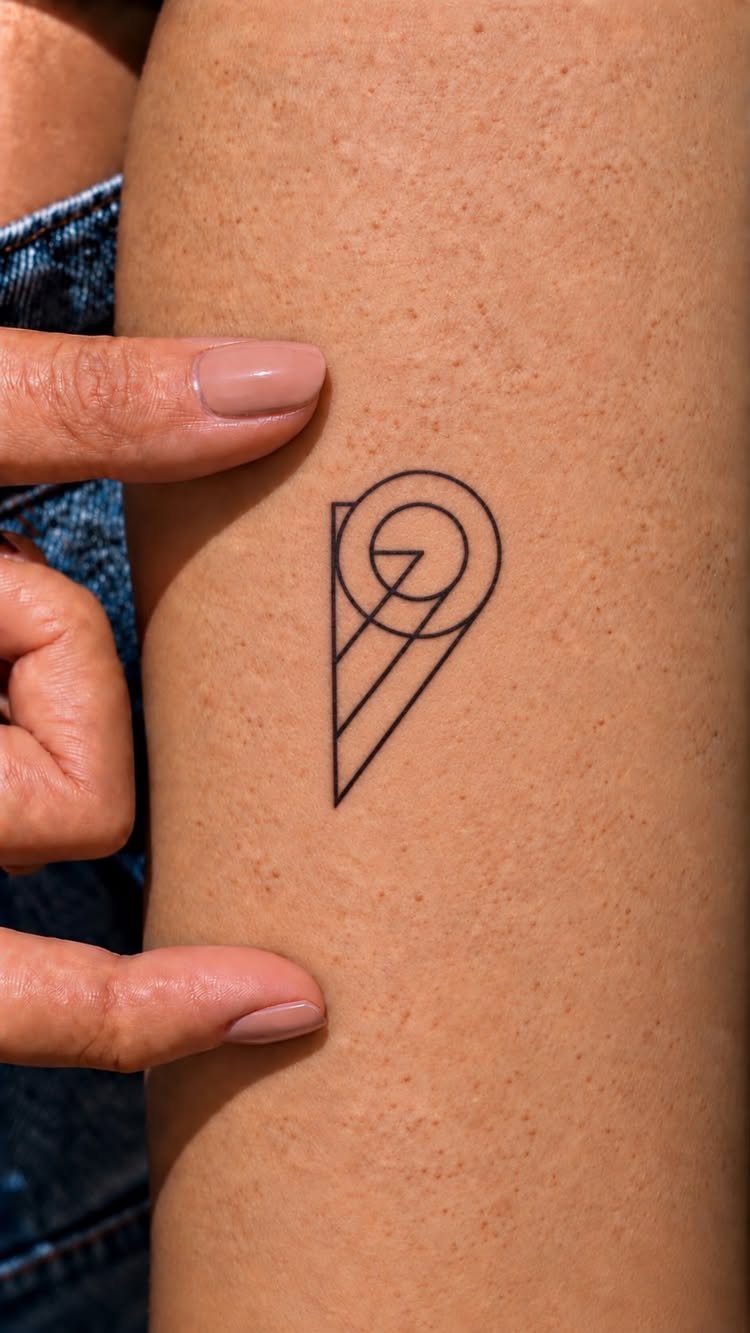 A small black ink geometric tattoo on a person's arm held by fingers.