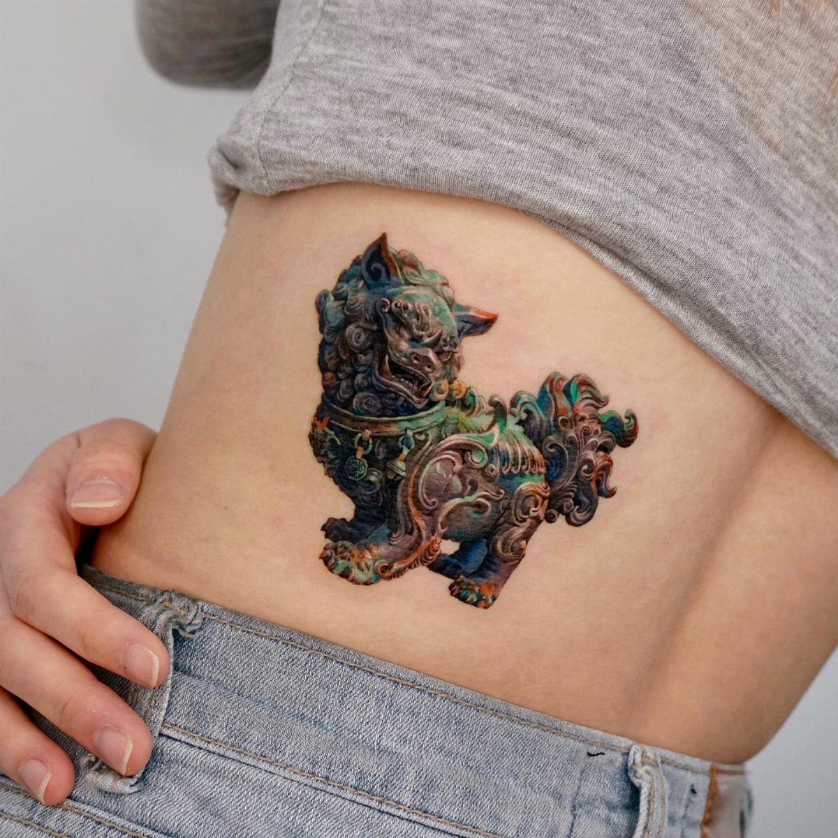 A colorful Haetae mythical creature tattoo on a person's lower side back skin.
