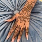 A hand and forearm adorned with intricate brown henna floral and geometric patterns.