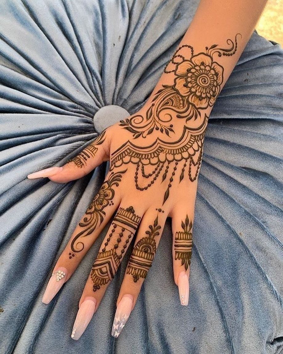 A hand and forearm adorned with intricate brown henna floral and geometric patterns.