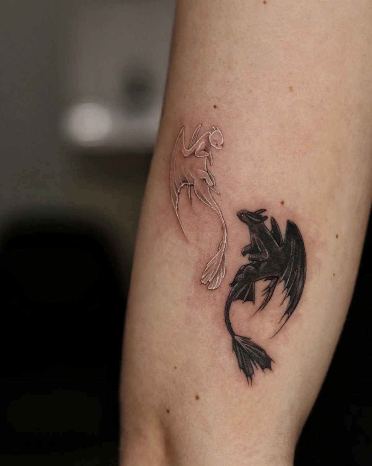 Two dragon tattoos, one in white ink and one in black ink, on a person's arm.