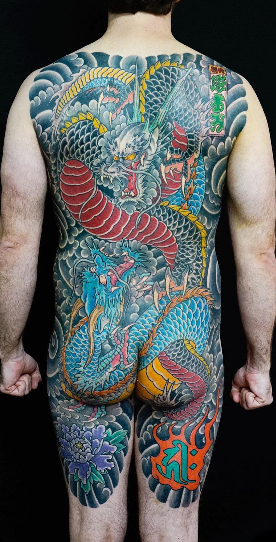 6 Dragon Backpiece Tattoo Ideas for Your Next Session 4 A man's back covered in a large, colorful Japanese-style dragon tattoo with clouds and flowers.