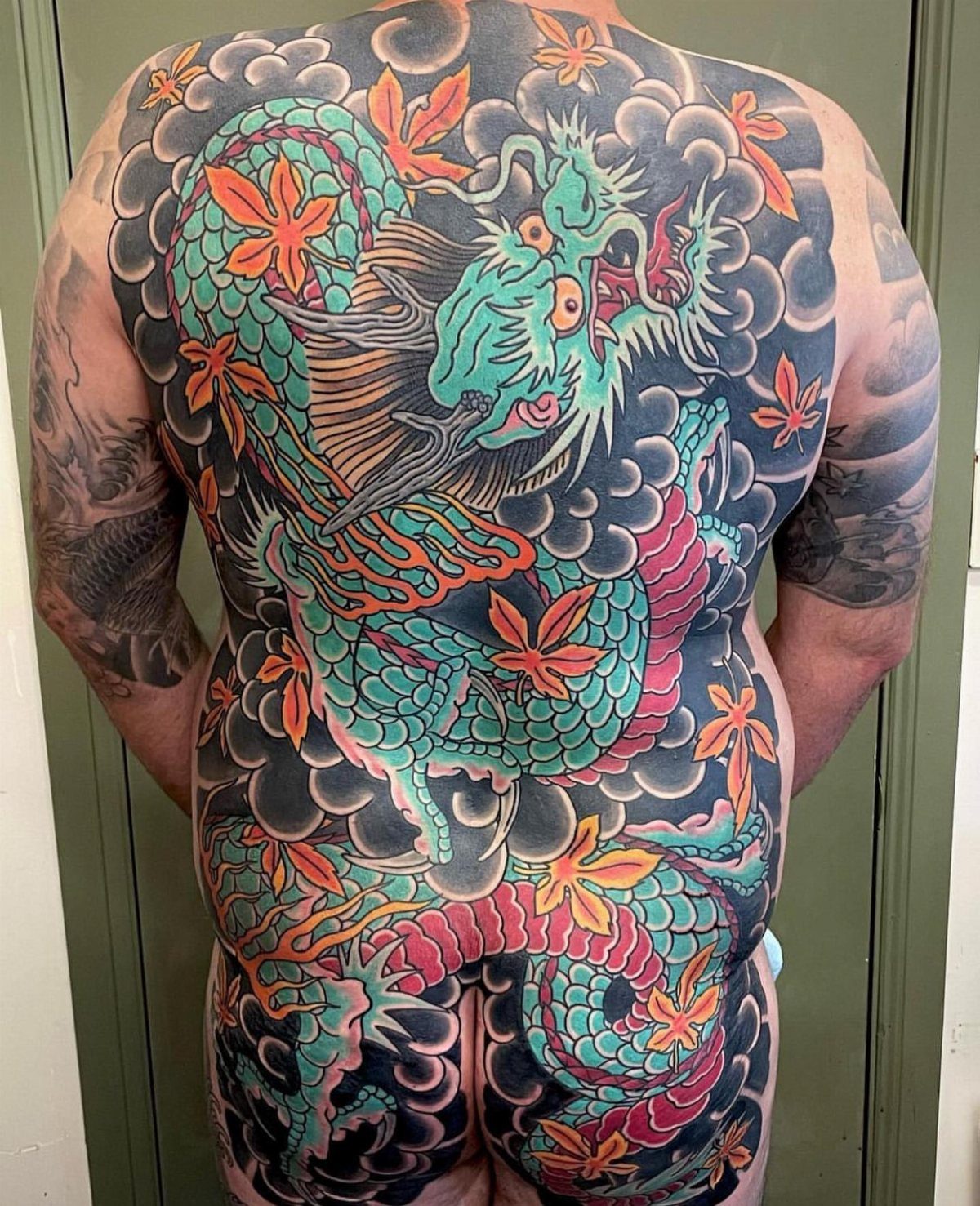 Back Pieces Tattoo: 7 Designs That Use the Whole Canvas 7 A person's back covered in a large, colorful dragon tattoo amidst dark clouds and maple leaves.