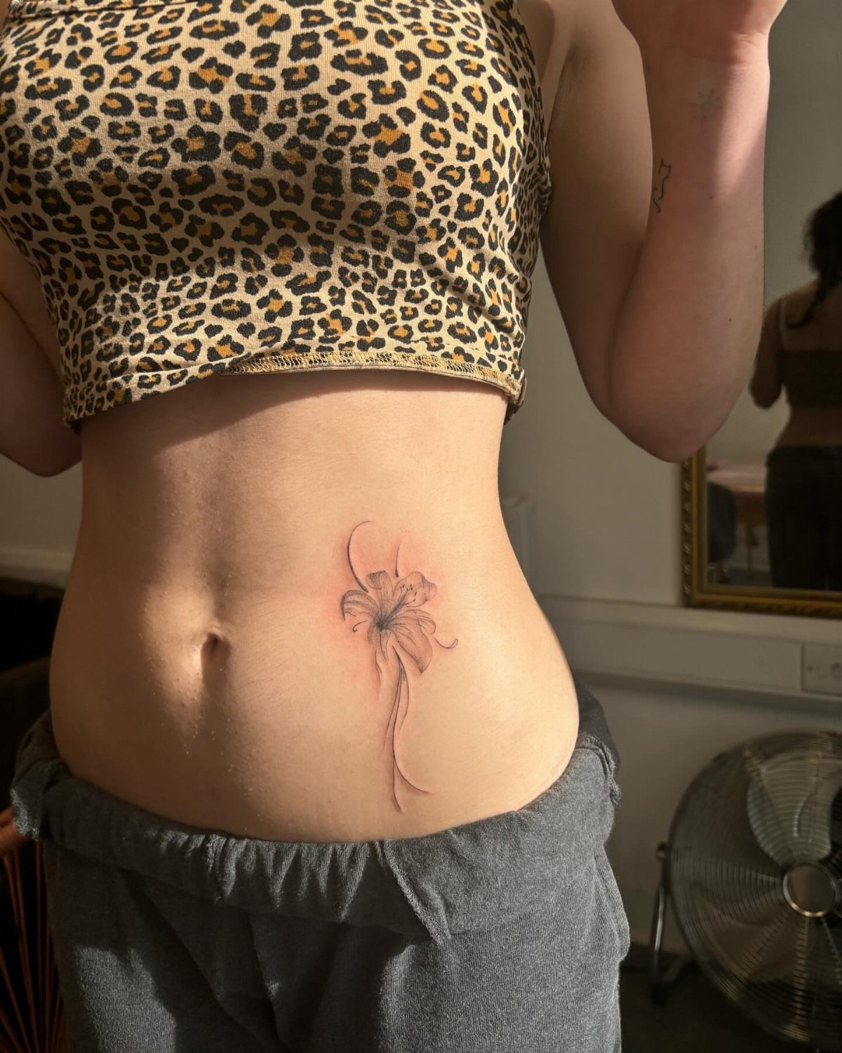 Tattoo Placement: 8 Lower Stomach Ideas for Your Next Ink 4 A delicate floral tattoo located on a person's lower stomach below a leopard print crop top.