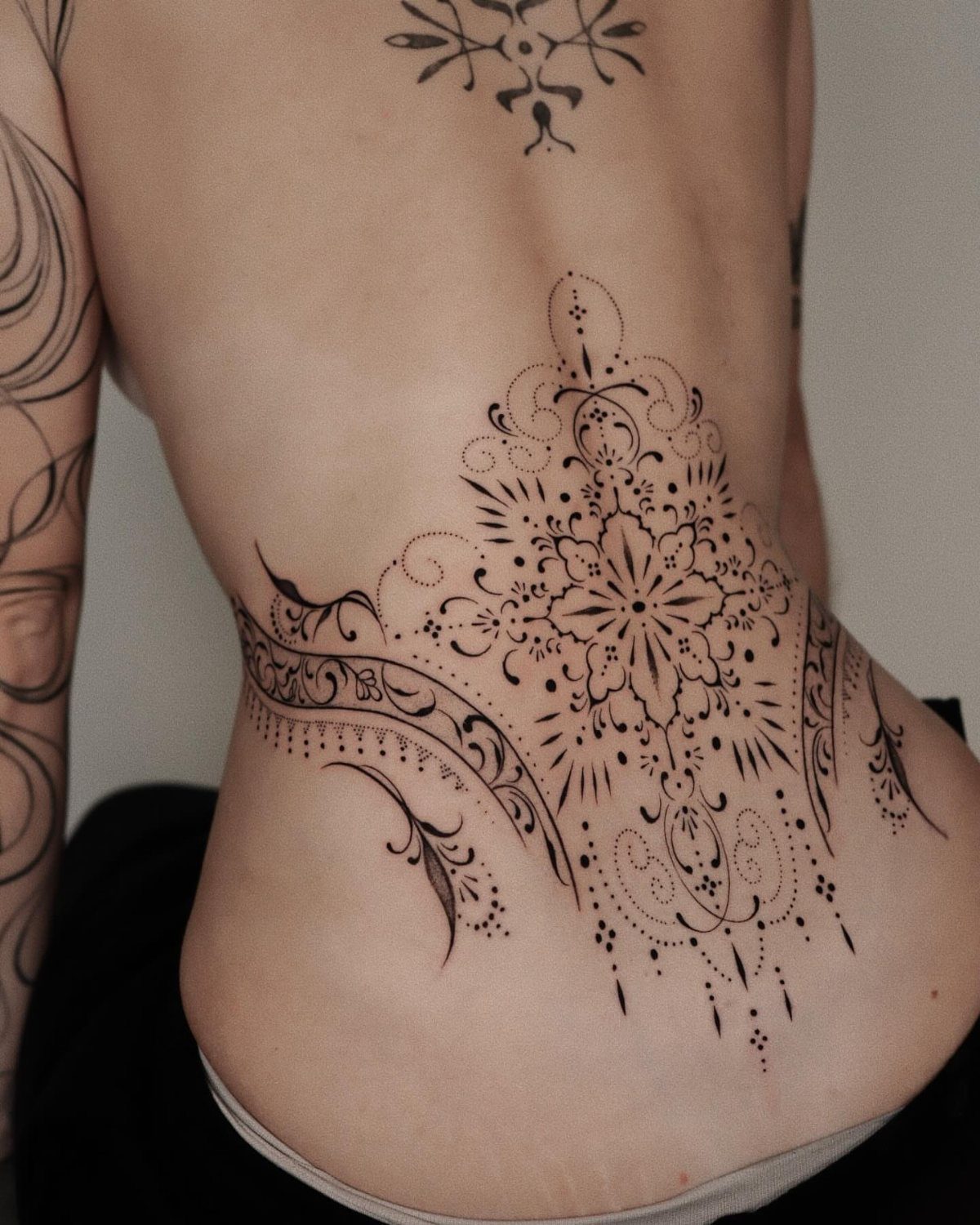 A large black ornamental mandala tattoo on a person's lower side back and hip area.