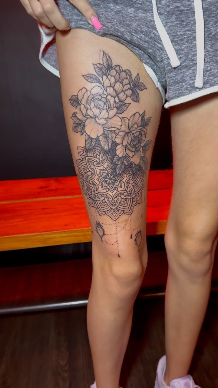 Thigh Tattoos for Women: 8 Ideas from Floral to Geometric Art 4 A large black ink tattoo with mandala patterns and peony flowers on a woman's thigh.