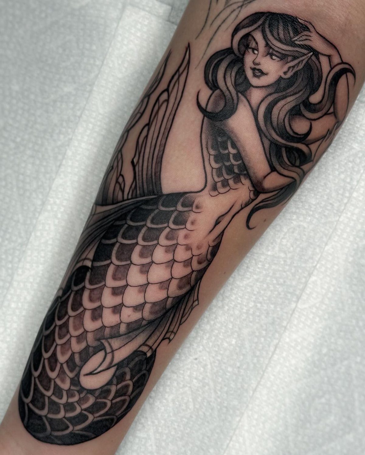 A black and grey mermaid tattoo with flowing hair and scales on a person's arm.