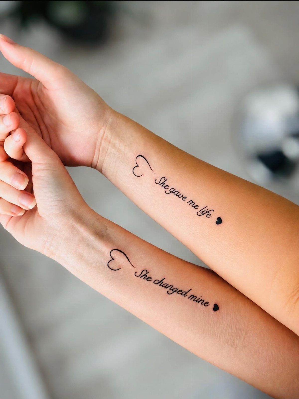 15 Tattoo Placement Heart Ideas for Meaning and Style 11 Two forearms side by side displaying small heart tattoos with sentimental text in black ink.