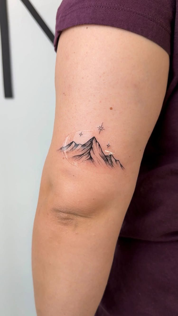 Fine Line Travel Tattoo: 10 Designs That Stay Light on Skin 5 A fine line tattoo of mountain peaks and stars on a person's arm.