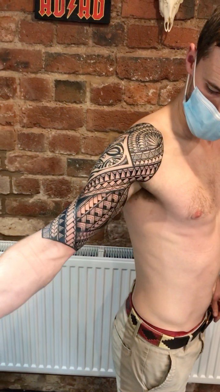 Polynesian Tattoo Pattern: 16 Island Styles From Marquesan to Maori 9 A man displaying a large, intricate black ink Polynesian tribal tattoo covering his entire arm.