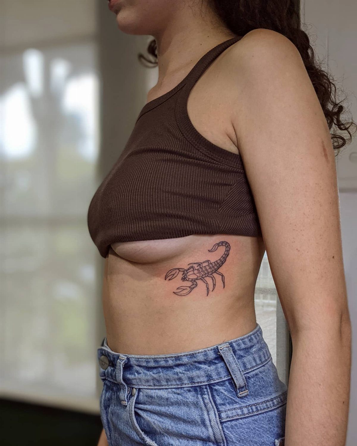 A person with a small black scorpion tattoo on their side ribcage area.