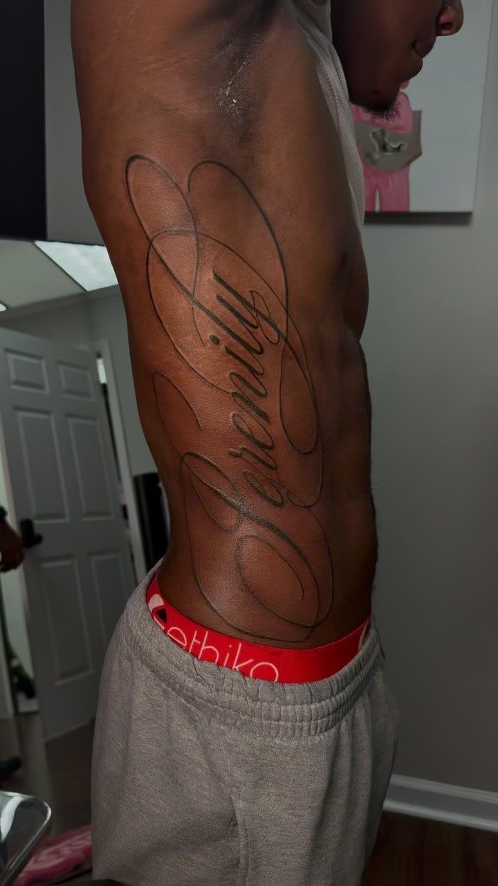 A person's side profile showing a large script tattoo reading Serenity on their ribs.