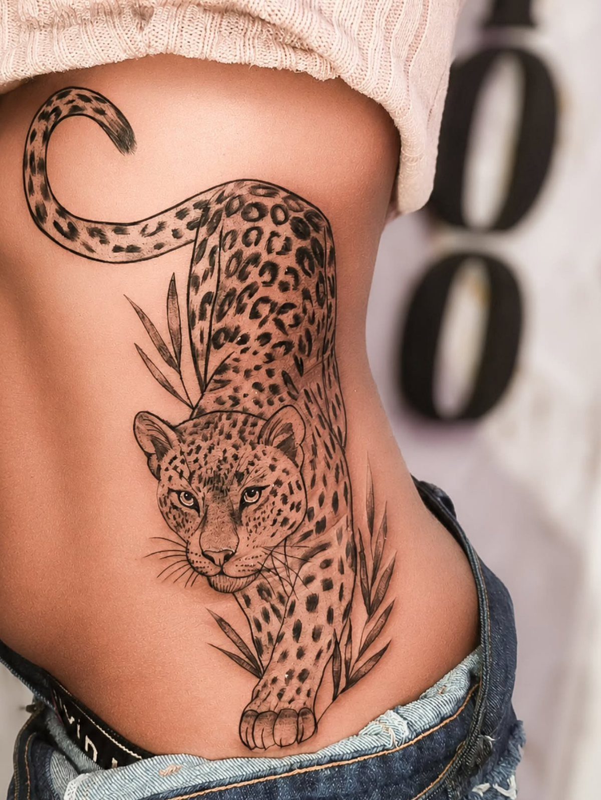 A leopard tattoo with leaf accents on a person's side ribs.