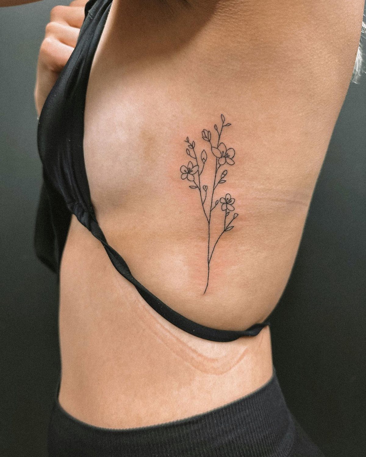 A delicate black ink floral tattoo on a person's side rib area.