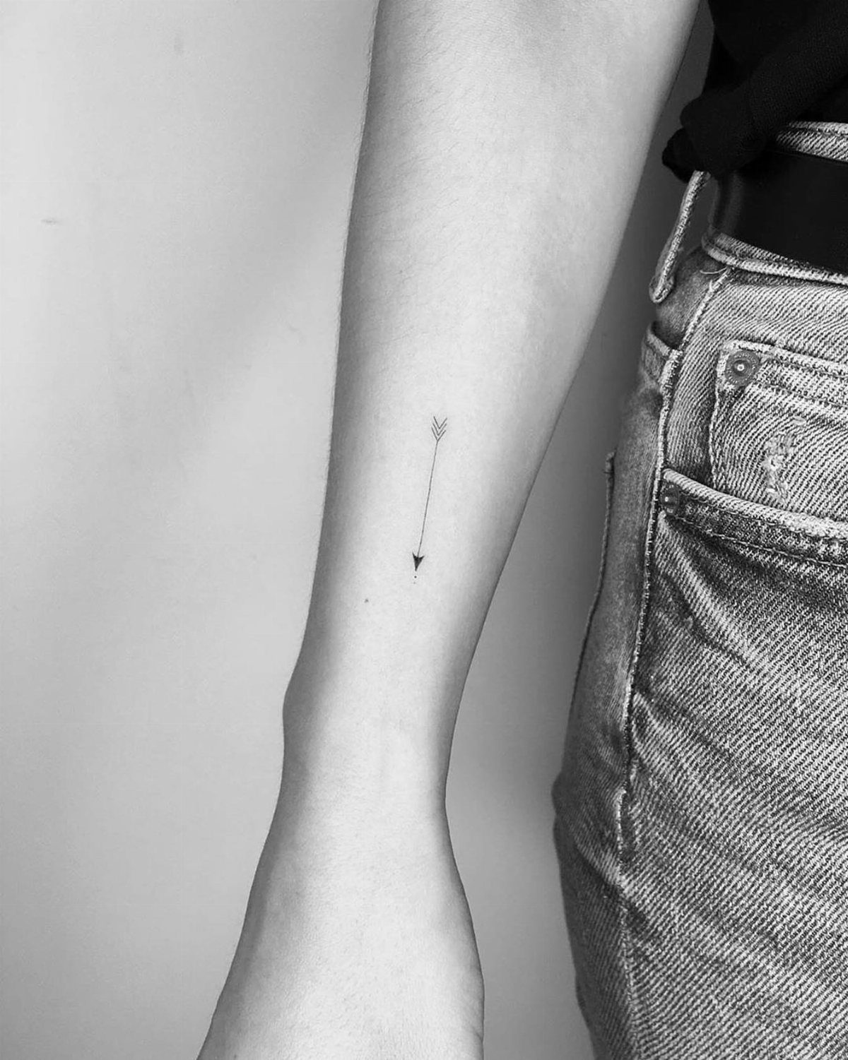 22 Delicate Tattoo Ideas for Light, Fine-Line Ink 8 A small, fine-line arrow tattoo on a person's forearm against a light background.