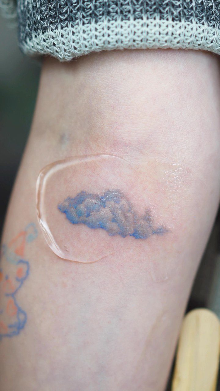 22 Delicate Tattoo Ideas for Light, Fine-Line Ink 22 A small blue watercolor cloud tattoo on skin under a clear bandage.