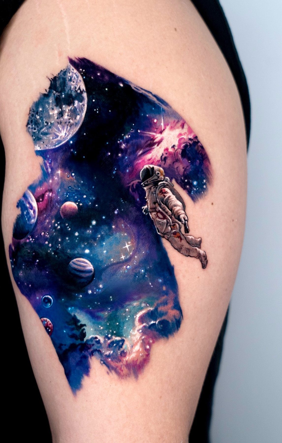 A detailed space themed tattoo on an arm featuring an astronaut and colorful planets.