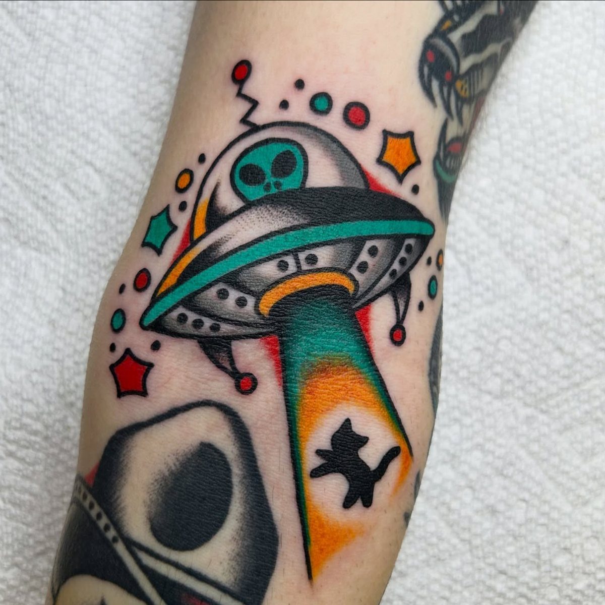 25 Space Themed Tattoos from Watercolor Cats to Black Holes 3 A colorful traditional tattoo of a UFO with a cat silhouette inside its tractor beam.