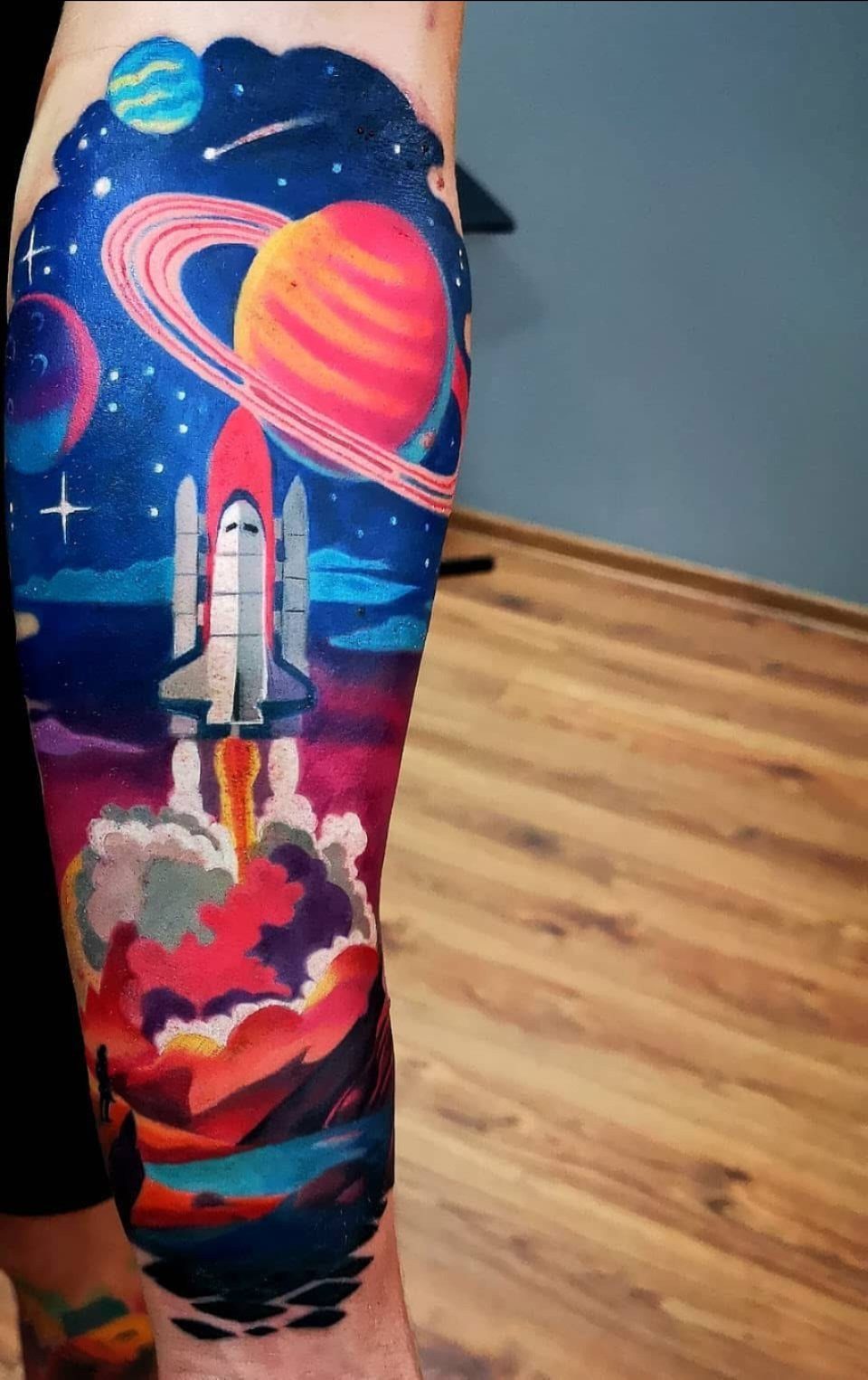 25 Space Themed Tattoos from Watercolor Cats to Black Holes 14 A vibrant space shuttle launch tattoo on a leg surrounded by colorful planets and stars.