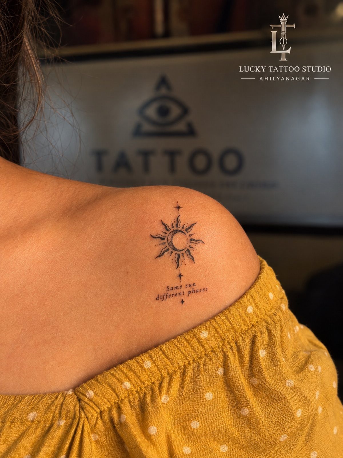 A small fine-line sun and moon tattoo on a person's shoulder with cursive text below.
