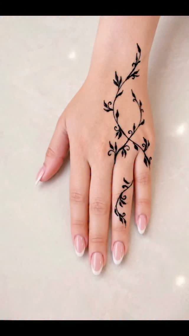 A hand decorated with a black henna tattoo featuring swirling vine and leaf patterns.